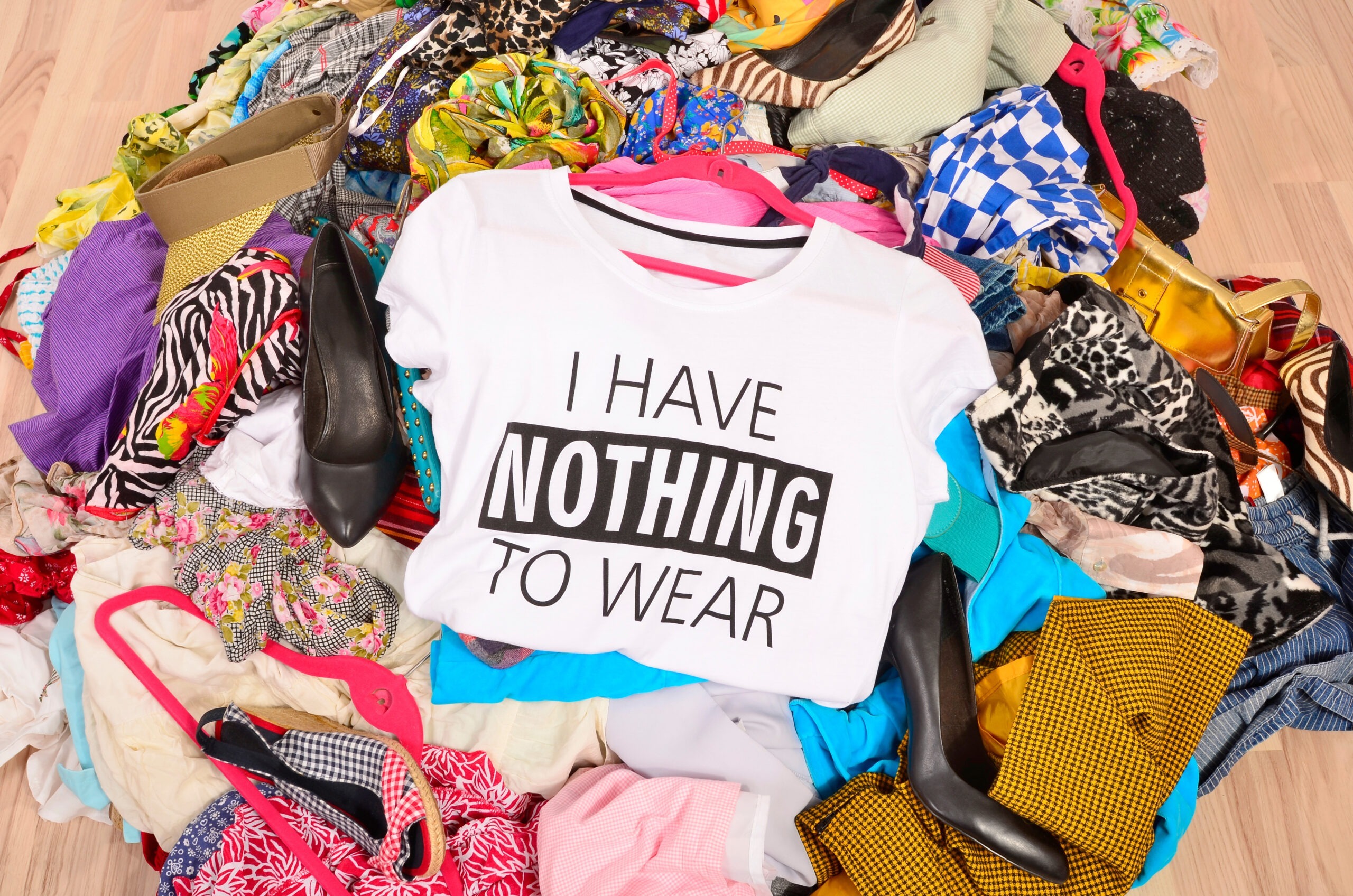 Tas de vêtements au sol avec au premier plan un t-shirt blanc avec le slogan anglais "I have nothing to wear", "Je n'ai rien à me mettre"